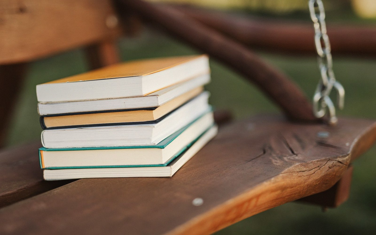 Stack of books with colored edges resting on a wooden porch swing bench