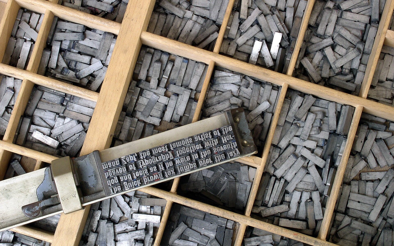 Metal movable type letters sorted in a wooden case with a composing stick of set text