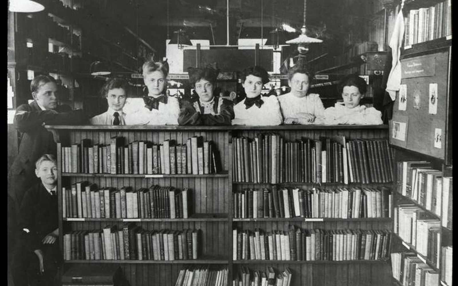 Library staff pose behind a book-filled counter in an early 20th-century circulating library
