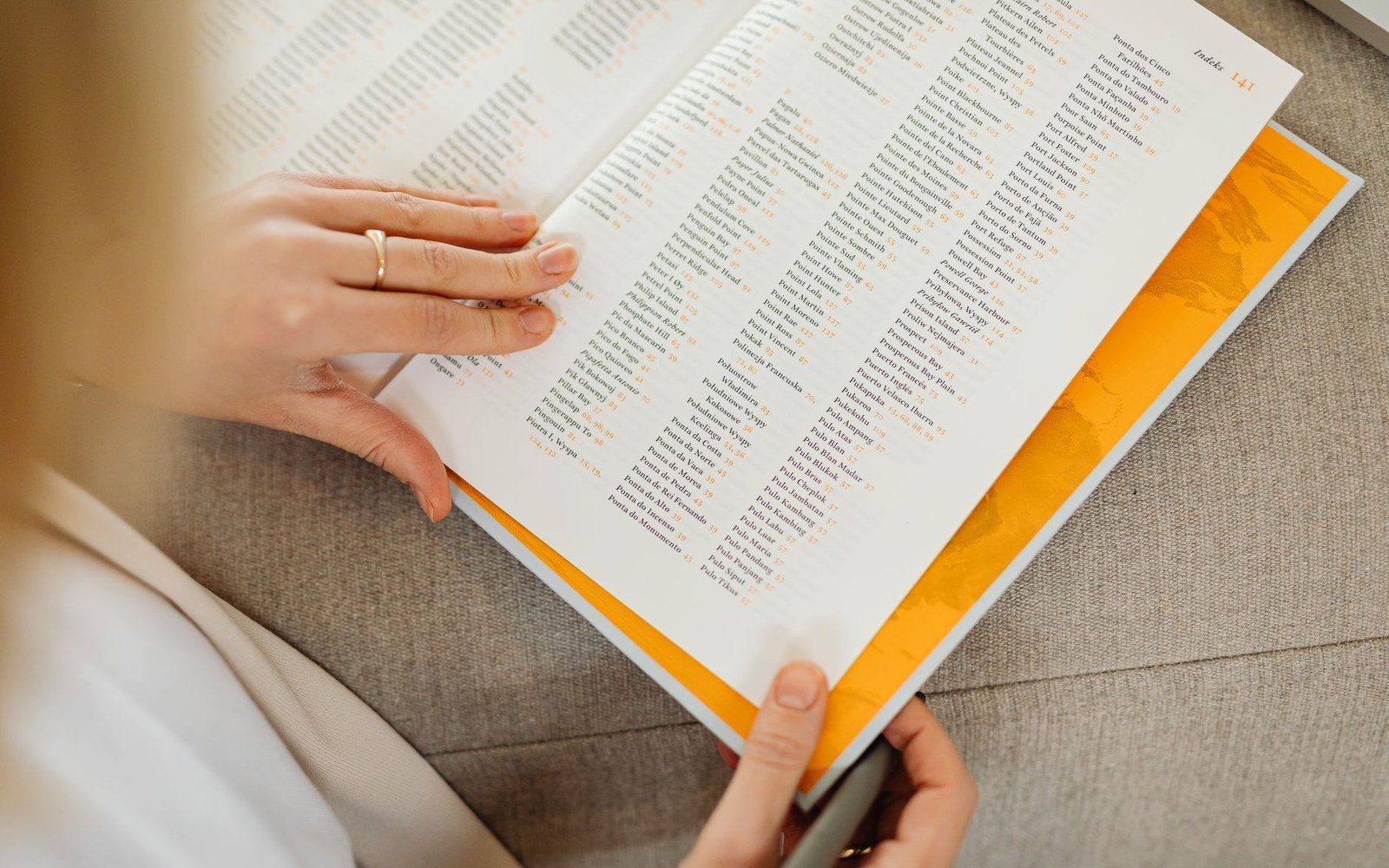 Hands flipping through a book's index pages with columns of entries and page numbers