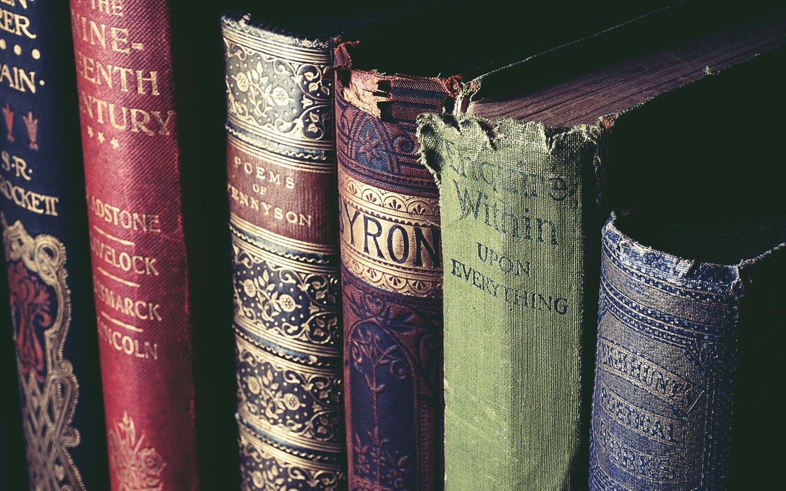 Worn spines of antique hardcover books, including titles by Tennyson and Byron, on a shelf